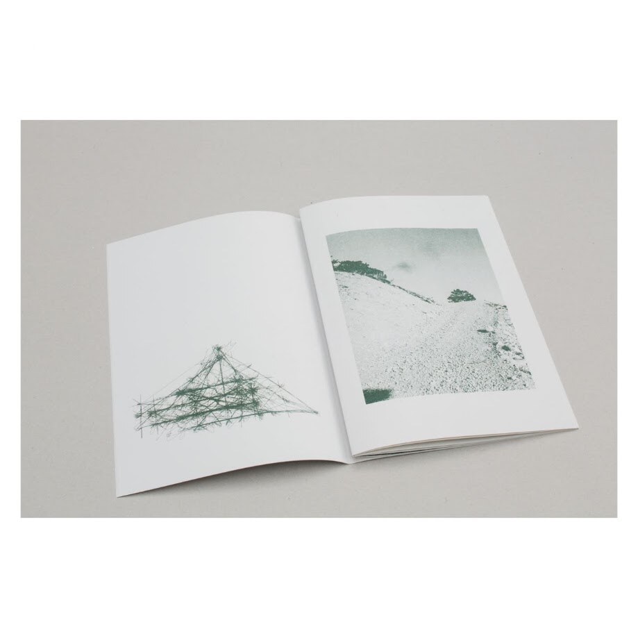 Book opened on a table. Left page: a green wireframe of a triangular scaffold. Right page: a duotone photograph of a bare hillside, a single tree at the ridge.