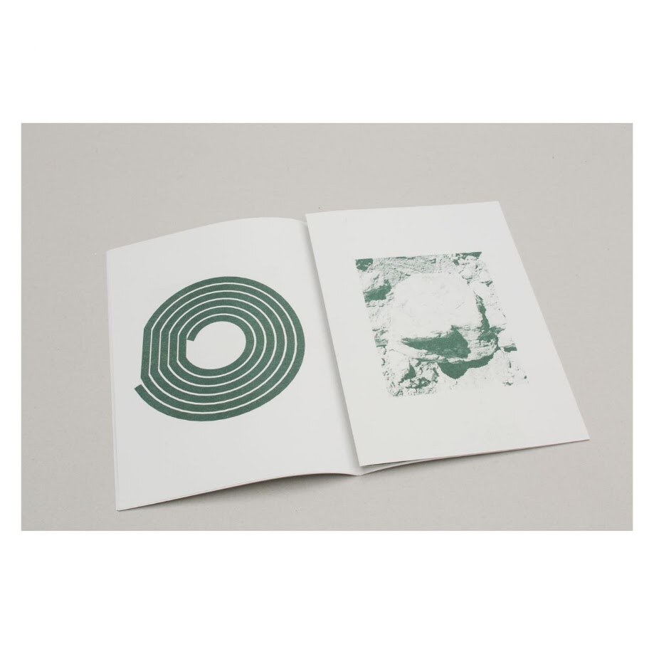 Book opened on a table. Left page: the concentric-circle glyph. Right page: a duotone photograph of exposed rock and scree.